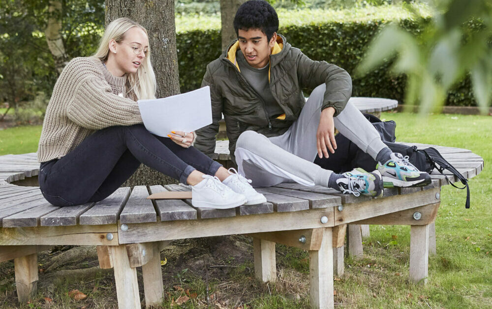 En ung kvinde og en ung mand sidder på en bænk og studerer