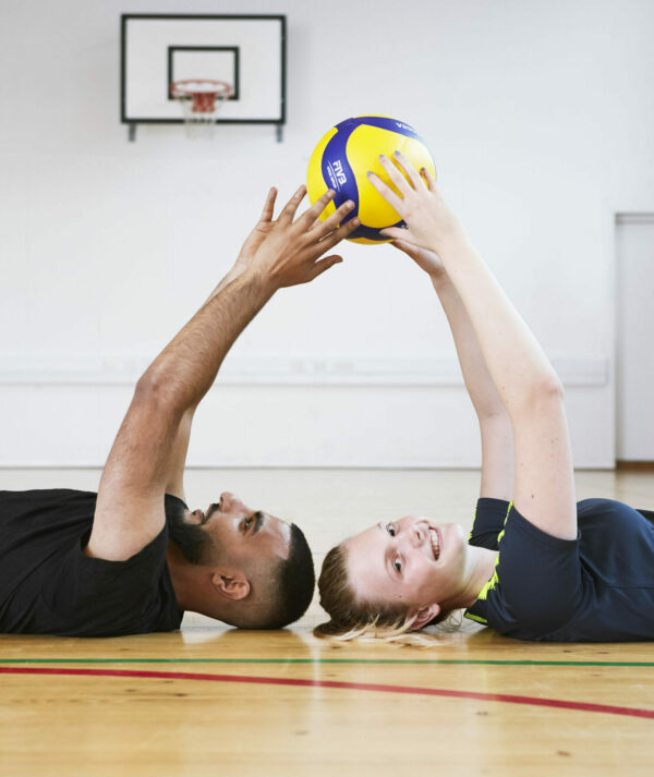 To studerende holder en bold på gulv i gymnastiksall
